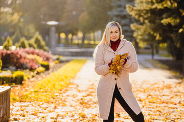 Romantic woman in the fall in the park. Stylish girl holding a golden autumn leaf near the face.