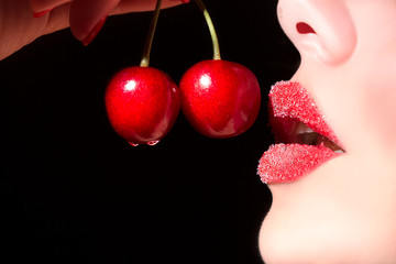 Beautiful young woman eating cherry. Sensual red lips in sugar isolated on black background.