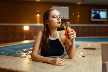 Sexy lady drinks fruit cocktail at the pool side