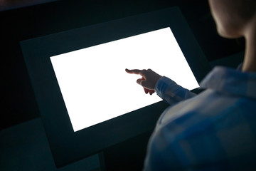Woman hand using white blank interactive touchscreen display of electronic multimedia kiosk in dark...