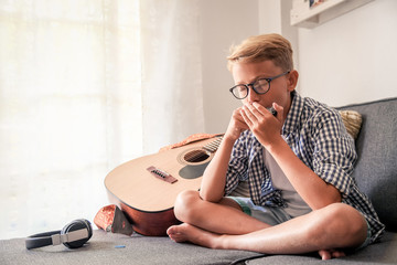 Beautiful young boy playing mouth harmonica. Music student exercises alone at home. Trendy...