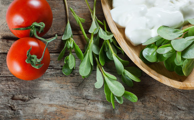 Fresh purslane (Portulaca oleracea), edible weeds with yoghurt and cherry tomatoes on wooden table....