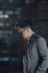 A shot from inside an office with a young business man wearing corporate formal attire looking down and tilting down his head. Shot behind window glass reflected with city lights.