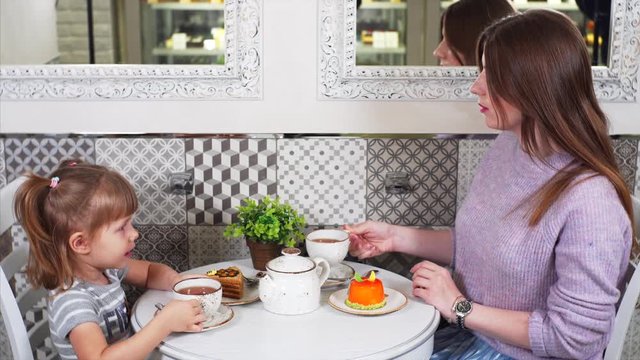 Sliding view of mother and daughter drinking tea with tasty pastry and honey cake in coffee shop