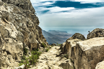Stony path at upland at sunny day. Clear lue sky and some clouds along the horizon line. Rocky road in dry mountain area. South of Tenerife. Canary Islands. Paintly