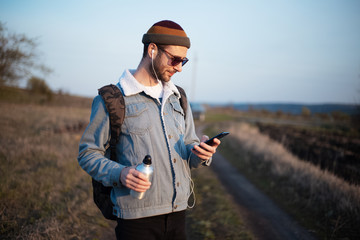 Portrait of young guy holding aluminium bottle with water and smartphone with earphones