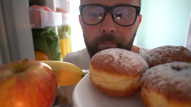 Young handsome caucasian man looking in fridge and takes a plate of cakes - concept 4k. POV from inside the refrigerator
