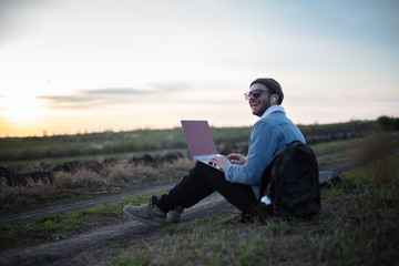 Smiling guy working on laptop with earphones on in the meadowlands 