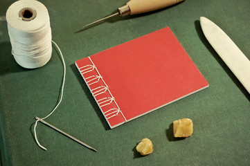Small Red Stab Stitch Book Surrounded by Bookbinding Tools
