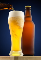 Beer is poured into a glass on the background of a bottle and a round blue gradient
