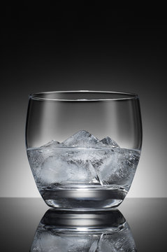 Water with ice cubes in a transparent glass on the background of a round gradient. Black and white image.
