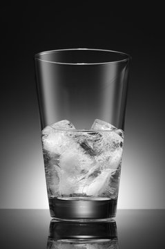 Water with ice cubes in a transparent glass on the background of a round gradient. Black and white image