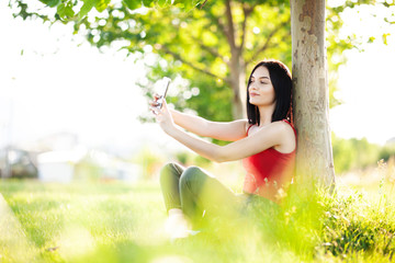 happy dark brown hair girl with her smartphone under a tree