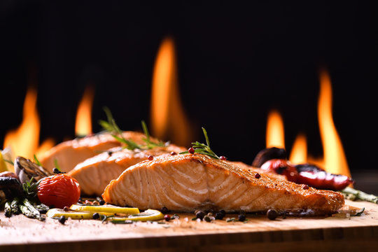 Grilled salmon fish and various vegetables on wooden table background