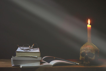 Candlestick skull, eyeglasses, pen and books on the wooden plank in dark night, Concept halloween day theme