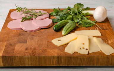 on the end cutting Board slicing of sausage and cheese with fresh cucumbers greens and a head of fresh garlic