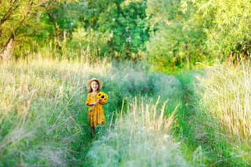 Little girl with a bouquet of wild yellow flowers standing in the meadow sunny summer day in a straw hat. Copy space