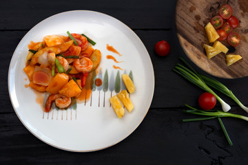Sweet and sour sauce fried with prawns on dark wood background.
