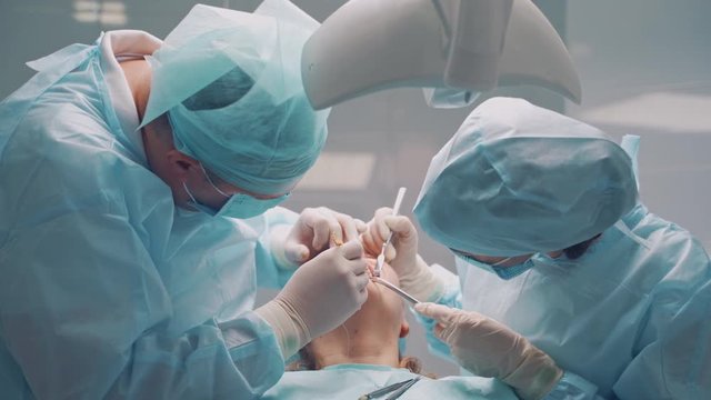 A male dentist in uniform perform dental implantation operation on a patient at dentistry office.