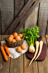 basket of eggs and carrots, parsley roots, celery, cutting board, old weathered wooden background