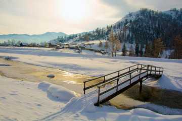 A bridge over a small creek, winter in the village, the ground under the snow.
