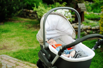 Baby boy in modern stroller on in a park.