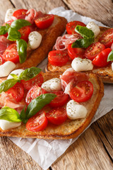Homemade toasts with mozzarella, tomatoes, prosciutto and basil close-up. vertical