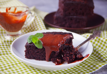 A piece of homemade chocolate cake on the plate with icing, mint leaf and chocolate spoon on the gray table