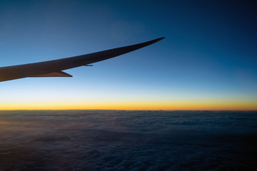 Fototapeta na wymiar Scene of Airplane wing over the cloud and fantastic sky at sunrise time when flying above the land, Nature and travel concept