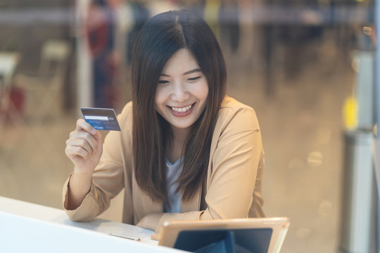 Asian woman using credit card with mobile phone for online shopping in department store over the clothes shop store background, technology money wallet and online payment concept, credit card mockup