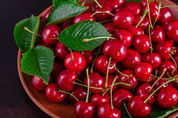 Sweet fresh organic cherry background close-up. Cherry in the plate with leaves on a dark background