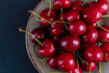 Sweet fresh organic cherry background close-up. Cherry in the plate with leaves on a dark background