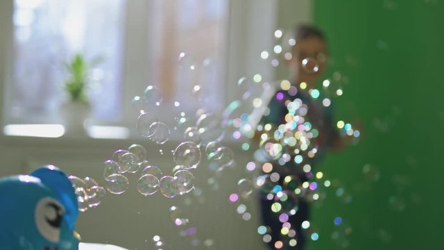 Many colorful bubbles flying in the room and a little boy playing with them. Joyful boy jumping happily and playing with soapy bubbles indoors. Soap bubbles show and a happy boy.