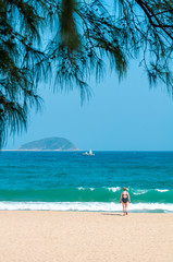 A young woman in a black closed swimsuit walks on a sandy sea beach.