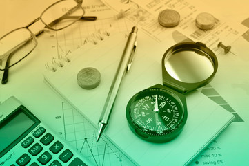 Compass, pen, coin, notebook, calculator and glasses on financial graph, Business investment concept
