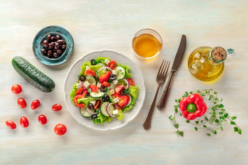 Greek salad with ingredients. An overhead photo of a plate of fresh salad with lettuce, feta cheese, tomatoes, cucumbers, onions and olives. A dinner with white wine