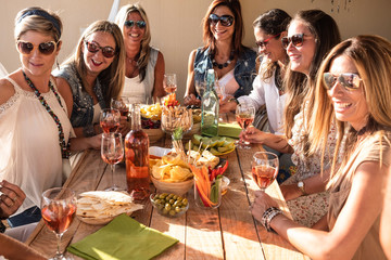 Wooden table full of appetizer and fruit. Group of beautiful people celebrate the party. Women smiling at the sunset sitted on the terrace