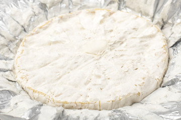 Camembert cheese with white mold in shiny foil. Snack to wine. Copy space