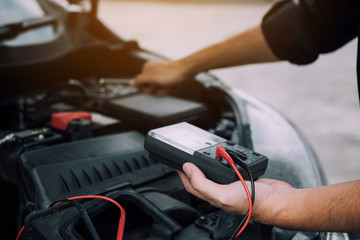 The car mechanic is carrying a battery meter and checking the general condition of the engine.