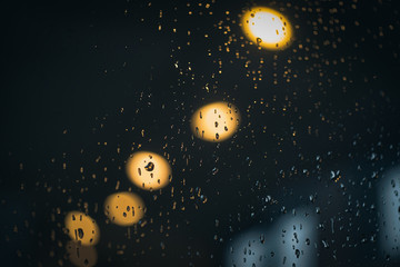 A series of light bulbs visible through a window glass on a rainy day