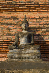 Ancient sculpture of a seated Buddha against a brick wall. Fragment of  ancient Buddhist temple Wat Mahathat. Sukhothai, Thailand