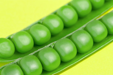 Fresh green pea pods and peas on the yellow background.