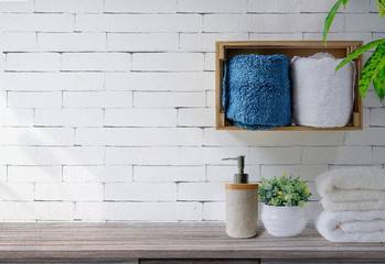 Clean towels with soap dispenser on shelf and wooden table in bathroom, white brick wall background.