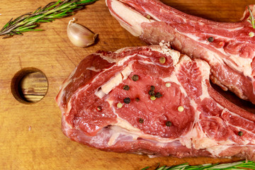 Raw fresh beef rib eye steak on bone with spices, garlic and rosemary on wooden table. Top view
