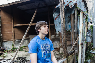 A handsome young boy sitting at the ruined house and looking up