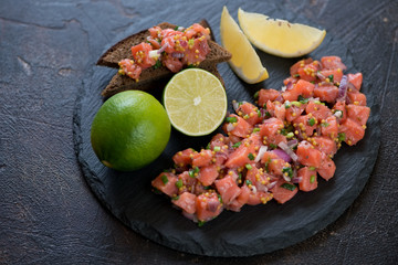 Salmon tartar served on a stone slate tray, studio shot over dark brown stone background
