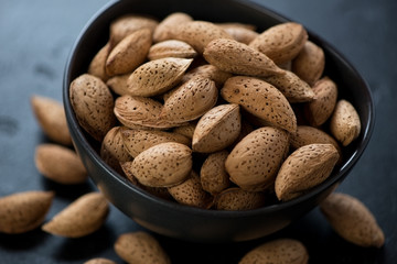Closeup of a black bowl with almond nuts, selective focus, studio shot