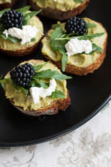 A gourmet lunch: guacamole sandwiches with cream cheese, blackberries and aragula.