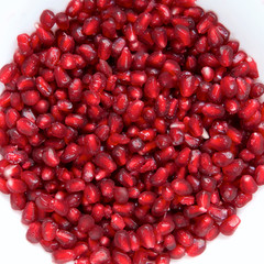 Red Pomegranate seeds on a dish with a white background.