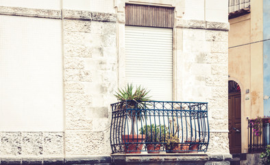 Balcony with flowerpots and house palm plants in a historic building in Acitrezza, Catania, traditional architecture of Sicily, Italy.